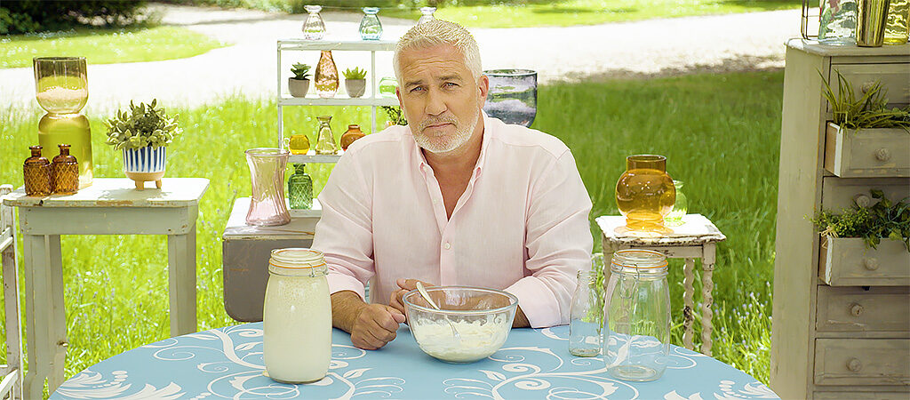 Paul Hollywood sitting at a table with his sourdough starter in a bowl and a jar