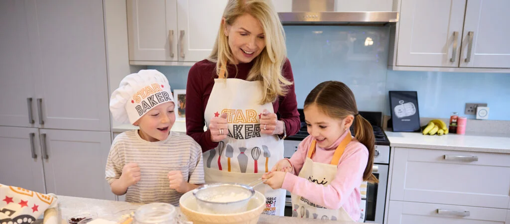A family bake while wearing Stand Up To Cancer chef's hats and aprons