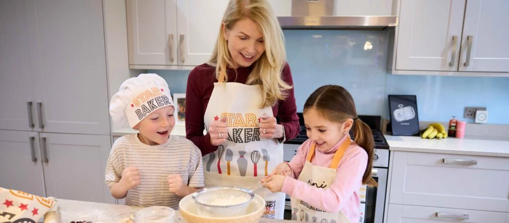 A family bake while wearing Stand Up To Cancer chef's hats and aprons